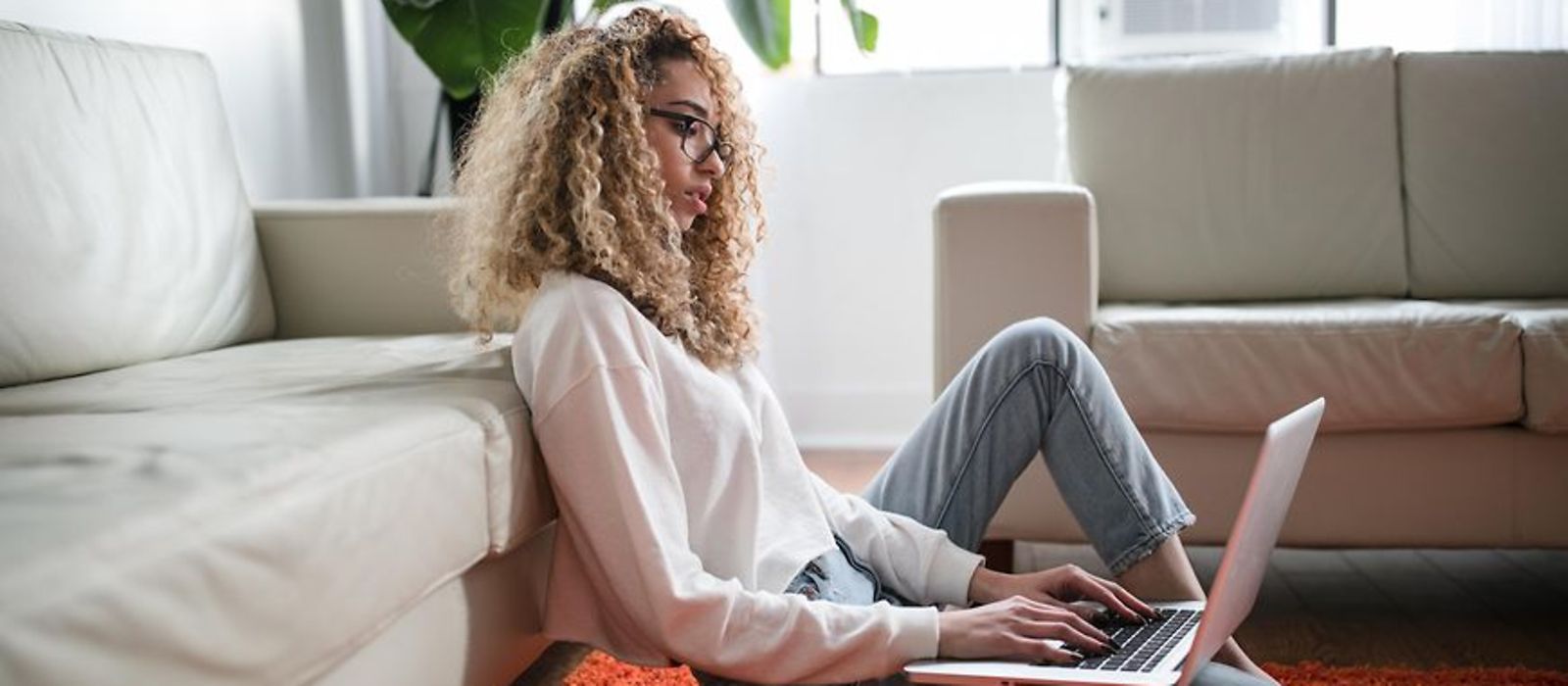 Frau sitzt zuhause auf dem Teppich und arbeitet am Laptop