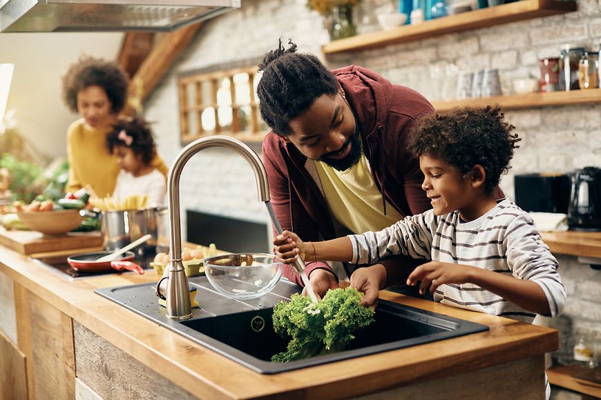 Mutter, vater und zwei kleine Kinder in der Küche, alle bereiten gemeinsam Essen zu