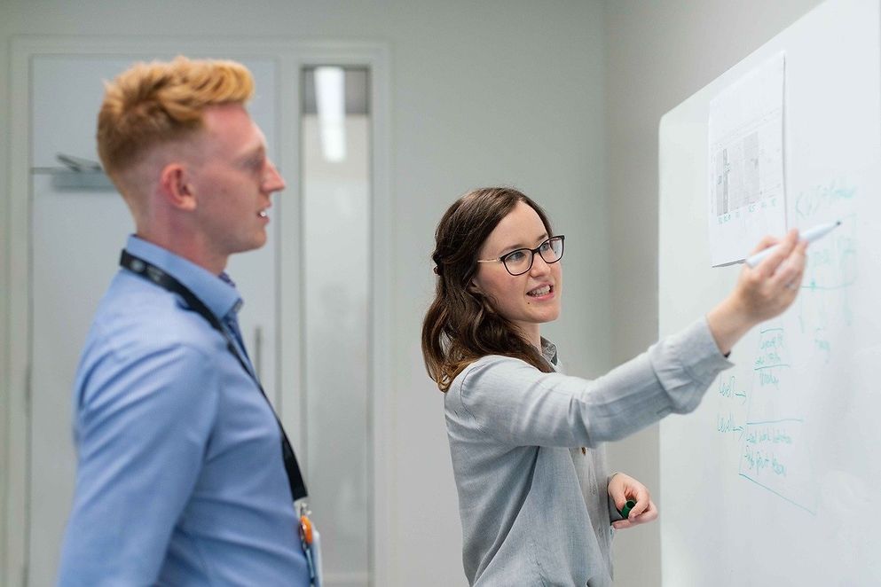 Frau demonstriert Mann an einem Whiteboard etwas