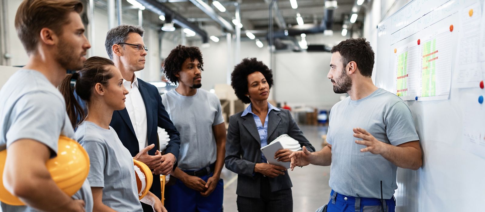 Männer und Frauen in Arbeitskleidung stehen vor einem Plan und besprechen etwas