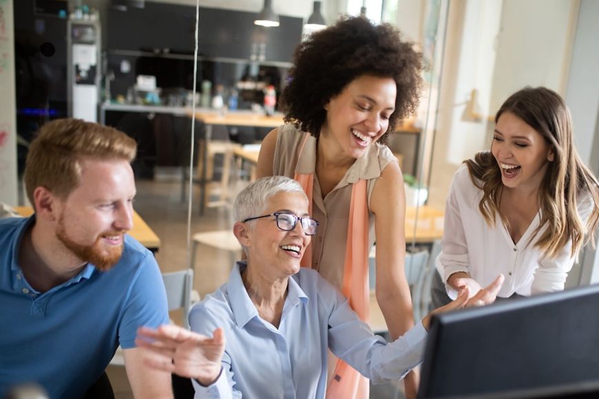 Mäner und Frauen unterschiedlichen Alters gucken gemeinsam auf einen Bildschirm und lachen