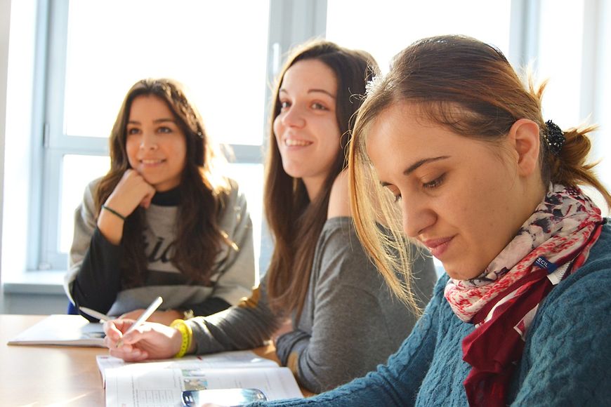 Drei junge Frauen sitzen am Tisch mit aufgeschlagenen Lehrbüchern