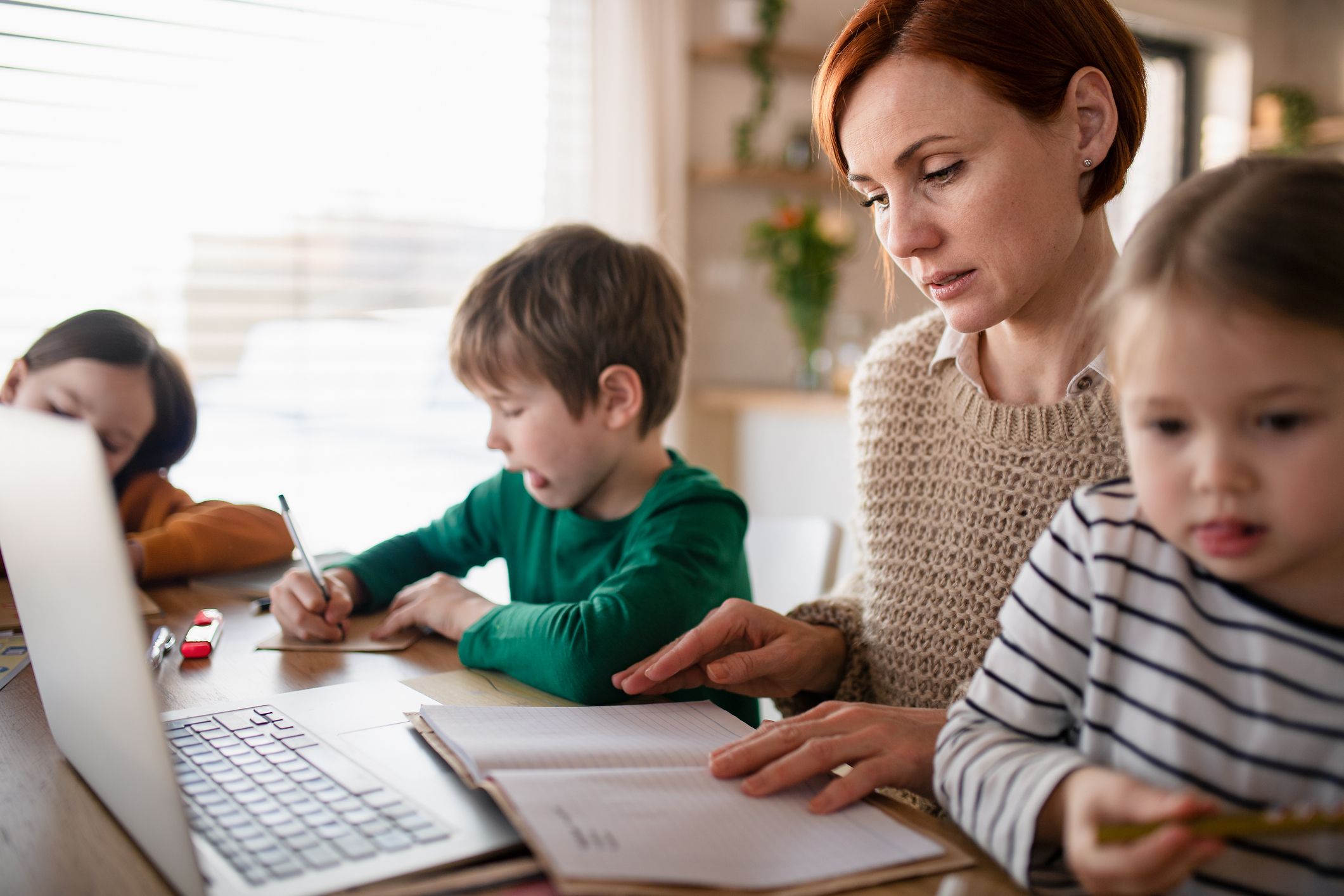 Mutter von kleinen Kindern, die beim Fernunterricht am Laptop arbeitet. 