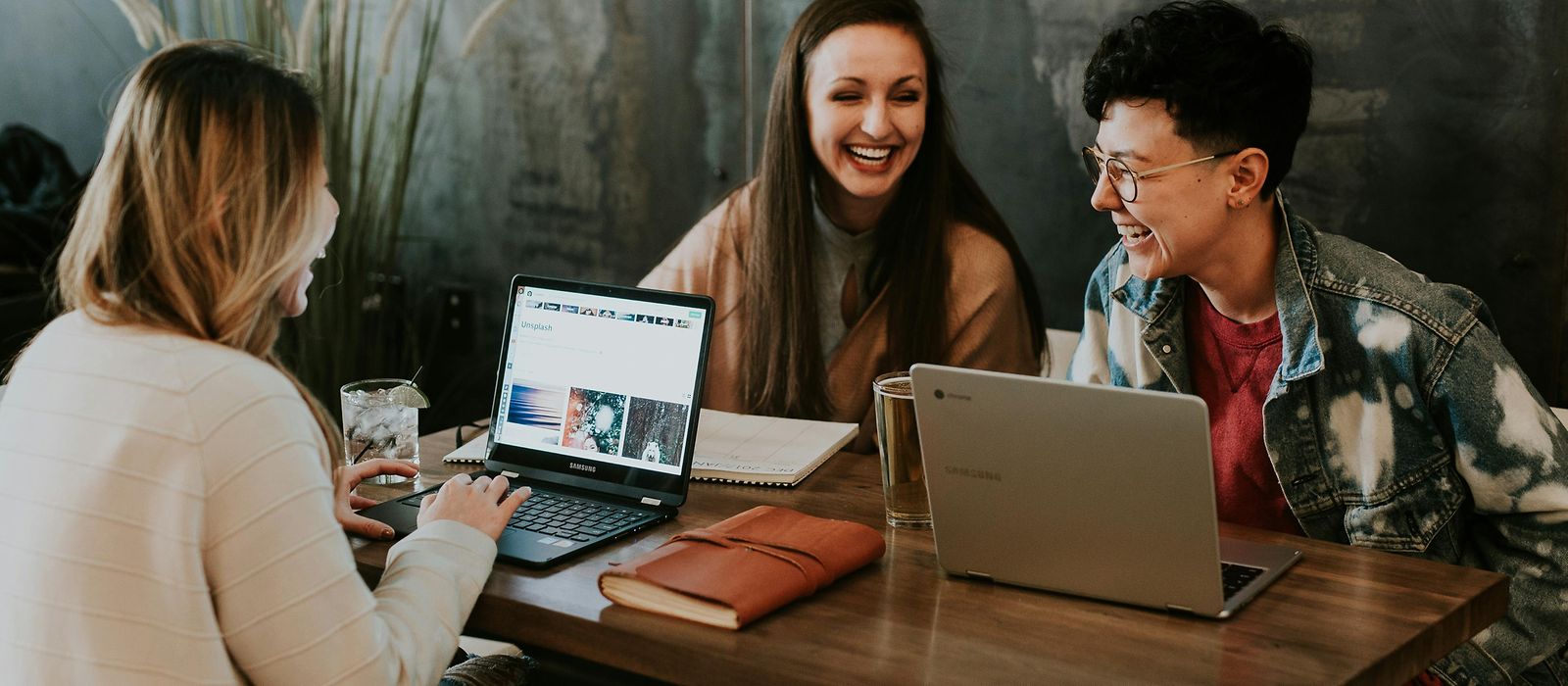 Drei Frauen sitzen mit Laptop am Tisch und lachen